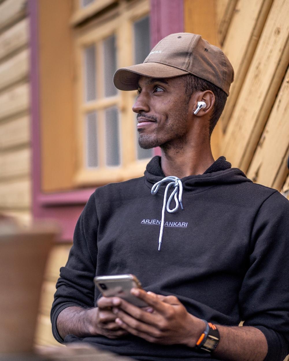 Mies nojaa lautaseinään lippalakki päässä ja kännykkä kädessä.