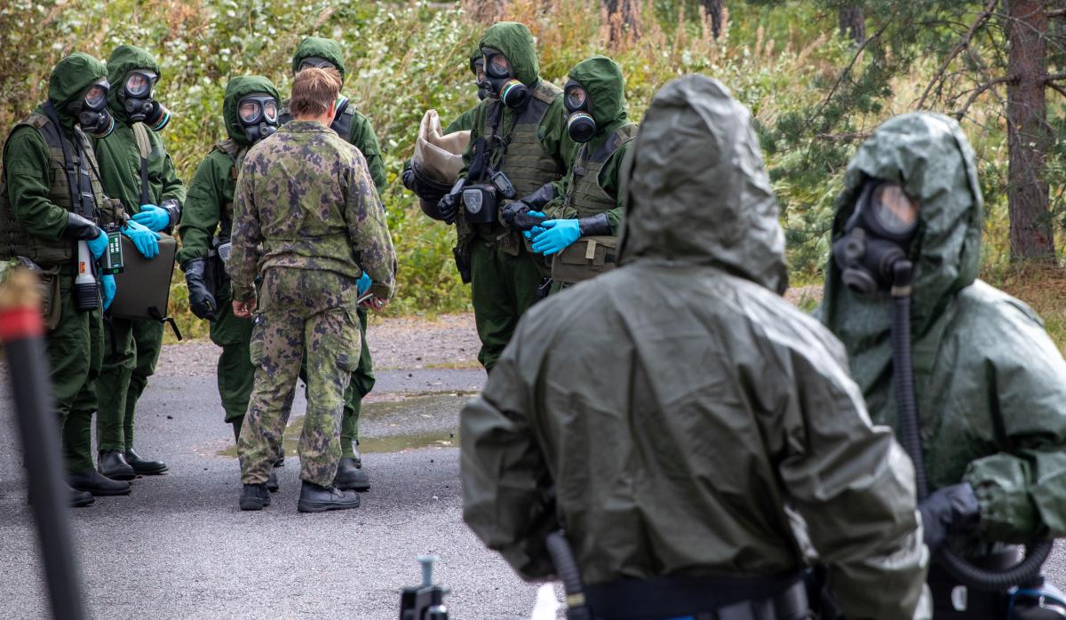 Kuvassa kahdeksan suojeluvarustukseen pukeutunutta reserviläistä ja yksi maastopukuun pukeutunut varusmies Suojelun erikoisosaston kertausharjoituksessa.