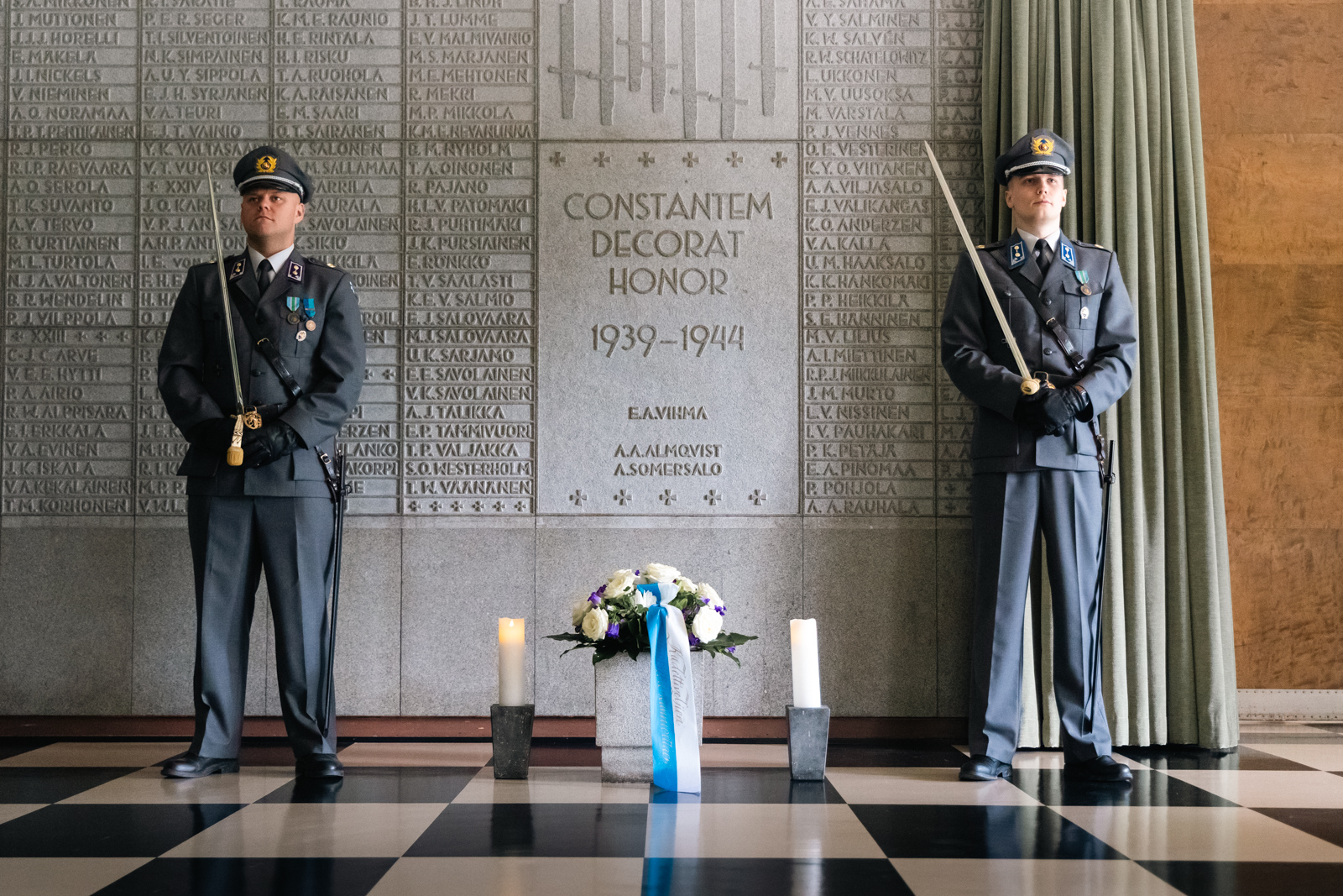 Kukkalaite, jonka ympärillä kaksi kynttilää ja kaksi kunniavartijaa Maanpuolustuskorkeakoulun sankariaulassa