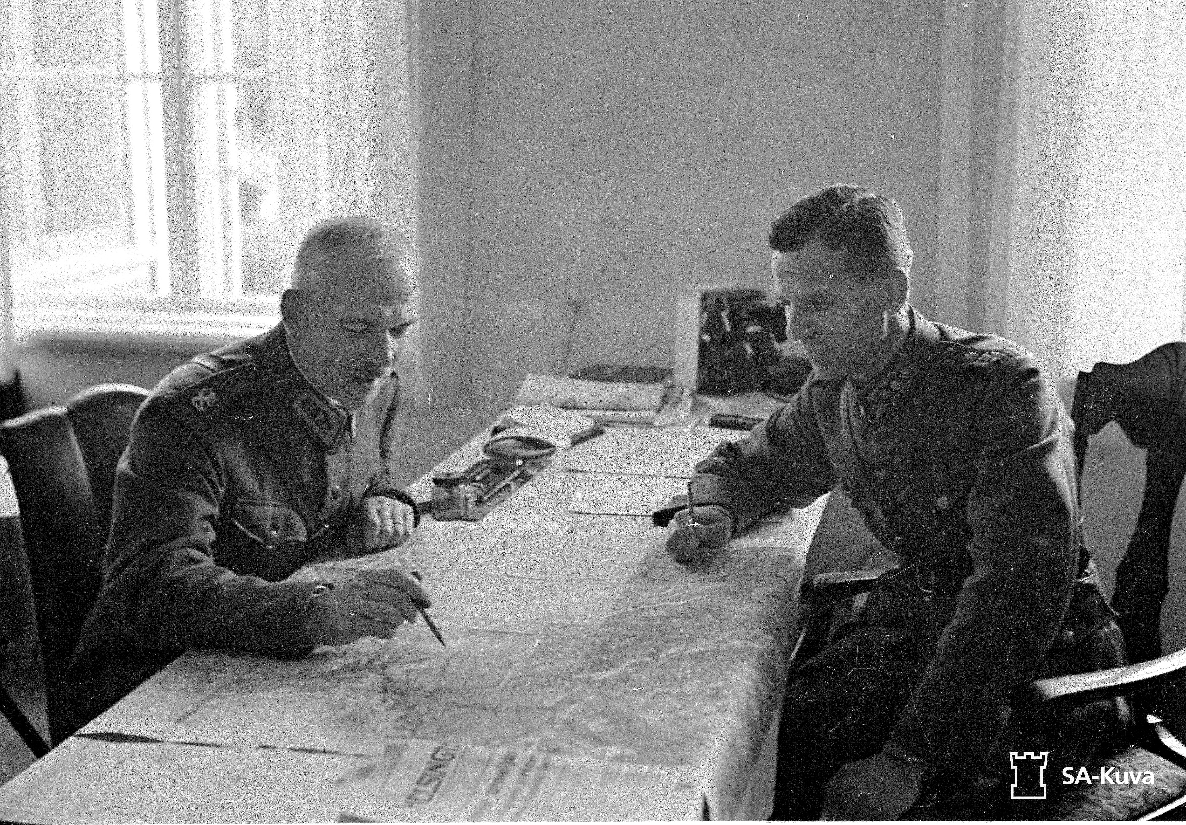 Kenraaliluutnantti Oesch ja eversti Vallo Nihtilä karttapöydän ääressä jatkosodan aikaan. Oesch pitelee kynää kädessään, Nihtilä katsoo karttaan päin. 
