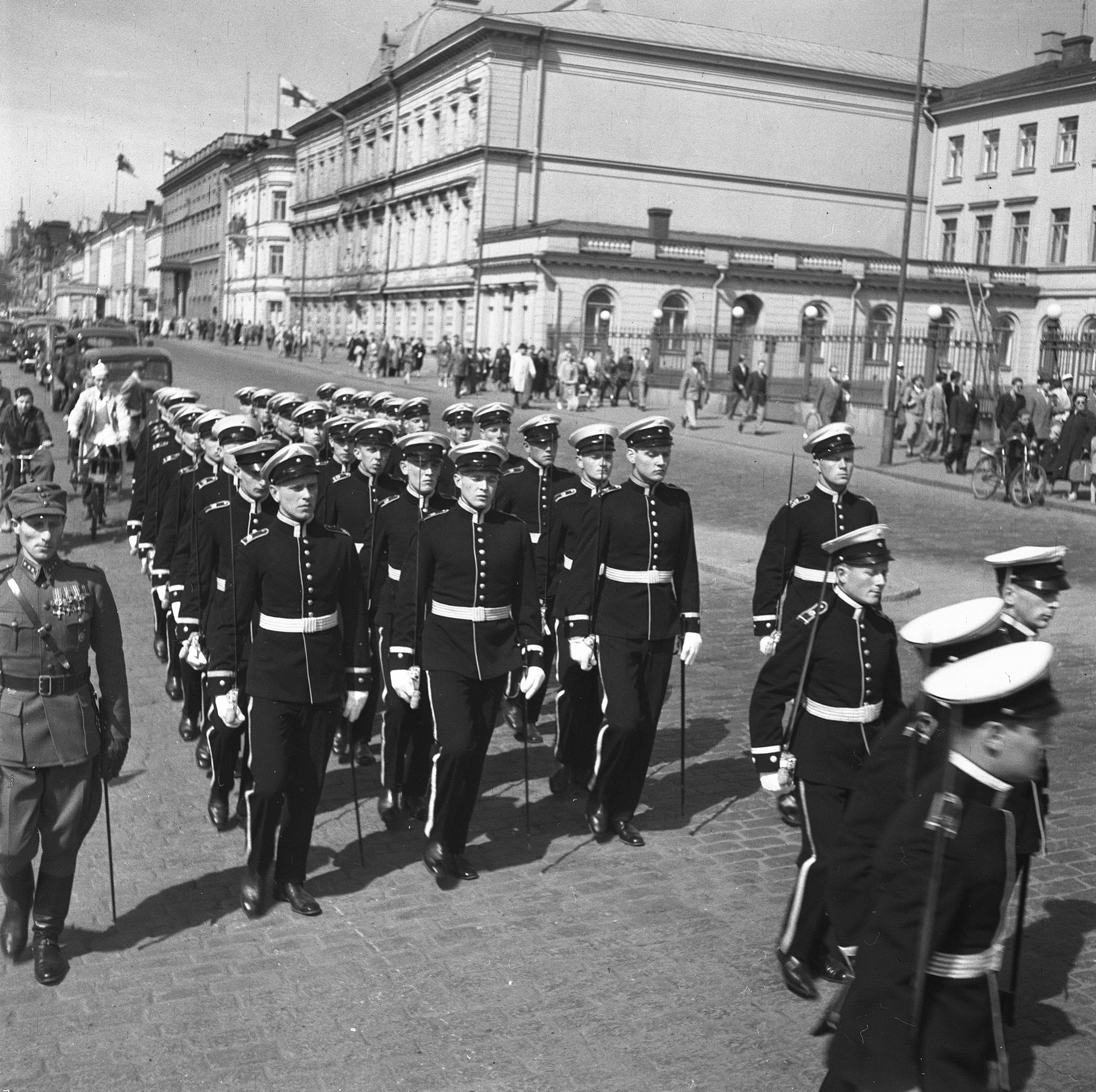 Kuvassa kadetit marssivat juhlapuvuissaan presidentinlinnan ohitse 50-luvun Suomessa.